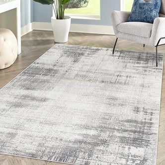 Franco 160x230cm Medium Tufted Contemporary Indoor Rug in an abstract gray-and-white pattern, complements the minimalist living room corner with a light gray armchair and green houseplant.