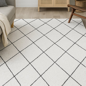 Milani 120x170cm Contemporary Printed Indoor Floor Rug with a black grid pattern on an off-white base, complementing a pale gray sofa and low wooden cabinet with woven front panels.