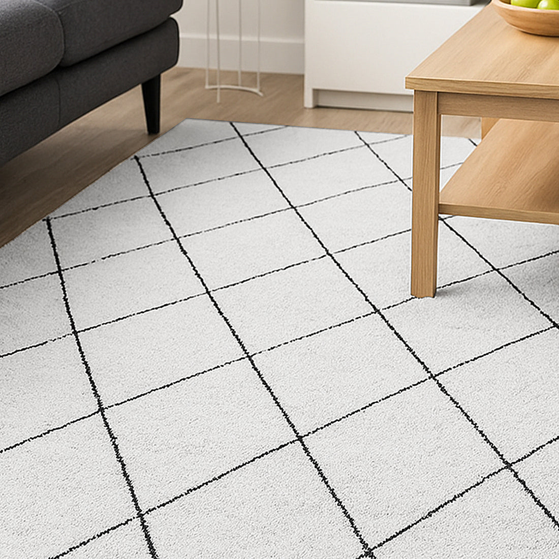 Milani 160x230cm Contemporary Printed Indoor Floor Rug features a simple black grid pattern on a white background, lying on a natural wood floor beneath a light-wood coffee table and dark gray sofa.