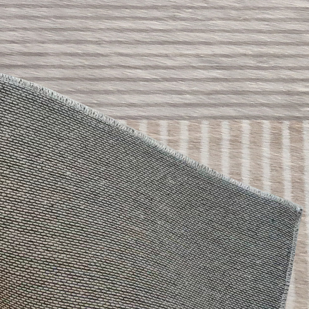 Close-up of the Olivia 120x180cm Polyester Tufted Modern Abstract Indoor Rug, showcasing its grey woven texture and serged edge on a light wood-grain floor, highlighting its contemporary style and craftsmanship.