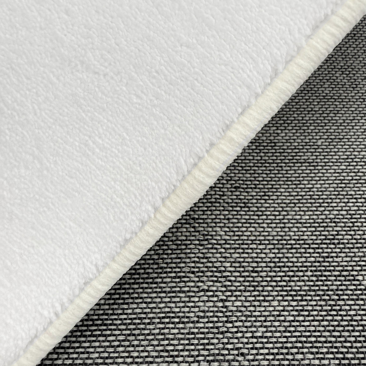 Close-up of Parna 200 x 300cm Curved Shaggy Rug in Cream White, showcasing soft, fleecy texture with overlocked border, layered over tightly woven gray fabric for contrast.