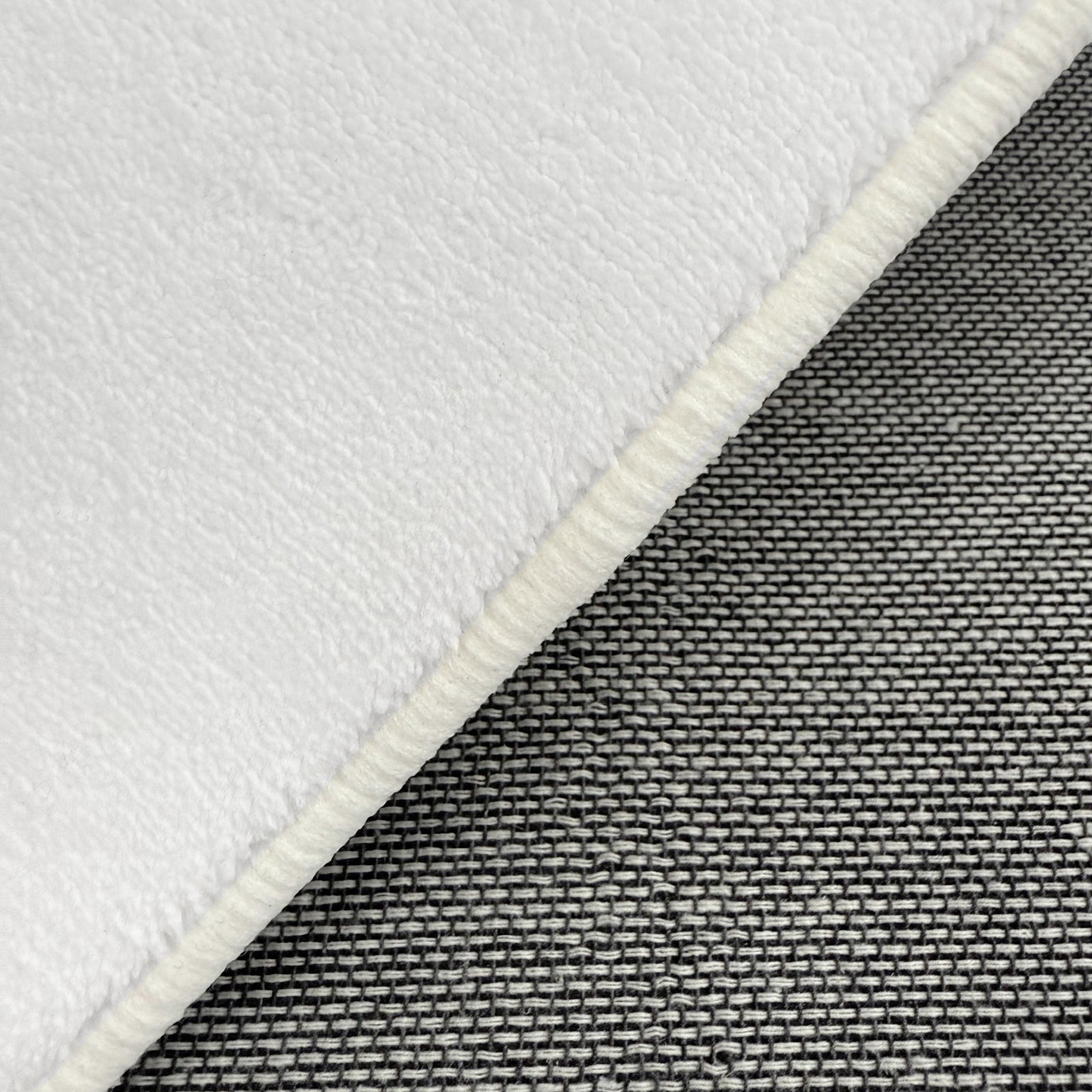 Close-up of Parna Curved 240x330cm Large Shag Rug in Cream White, showcasing the plush white fleece-like texture with a serged edge, overlaid on a grey basket-weave textile background.
