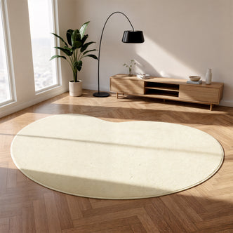 Parna Curved Large Soft Rug in Beige on herringbone wood floor, showcasing its unique organic shape and plush texture, complemented by a mid-century console, arched lamp, and potted plant.