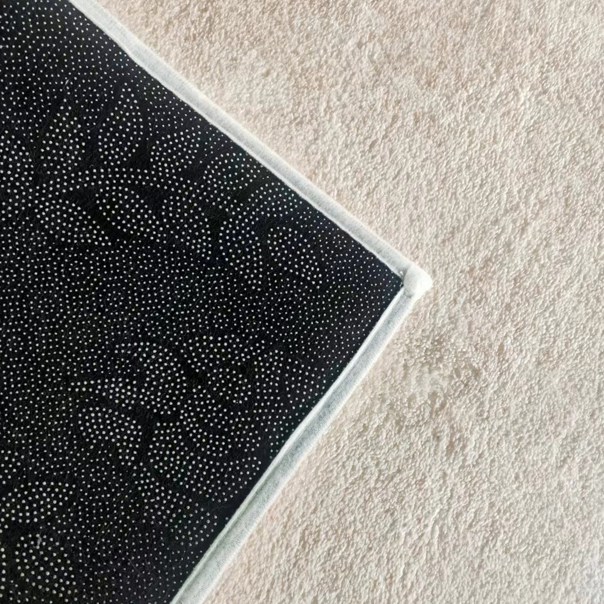 Close-up of Talbyn 160x230cm Medium Contemporary Abstract Floor Rug, showcasing a mandala-style pattern and white-stitched border on dark fabric, resting on a light, textured surface.