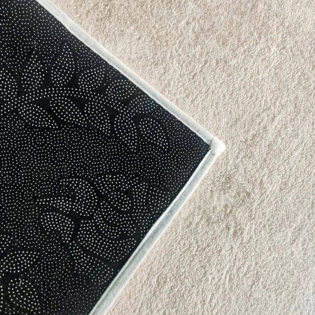 Corner of the Talbyn Contemporary Abstract Floor Rug 200 x 300cm, showcasing a non-slip silicone-dot pattern and white stitched border, lying on a light-colored carpet.