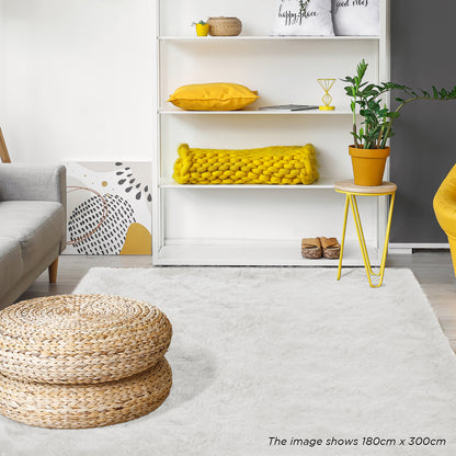 Zubuin Shaggy Plush Fluffy Rectangular Fur Rug - White 160 x 230cm, featured in a cozy living room, covers the floor beneath woven-straw poufs, complementing a light gray sofa and yellow accents.