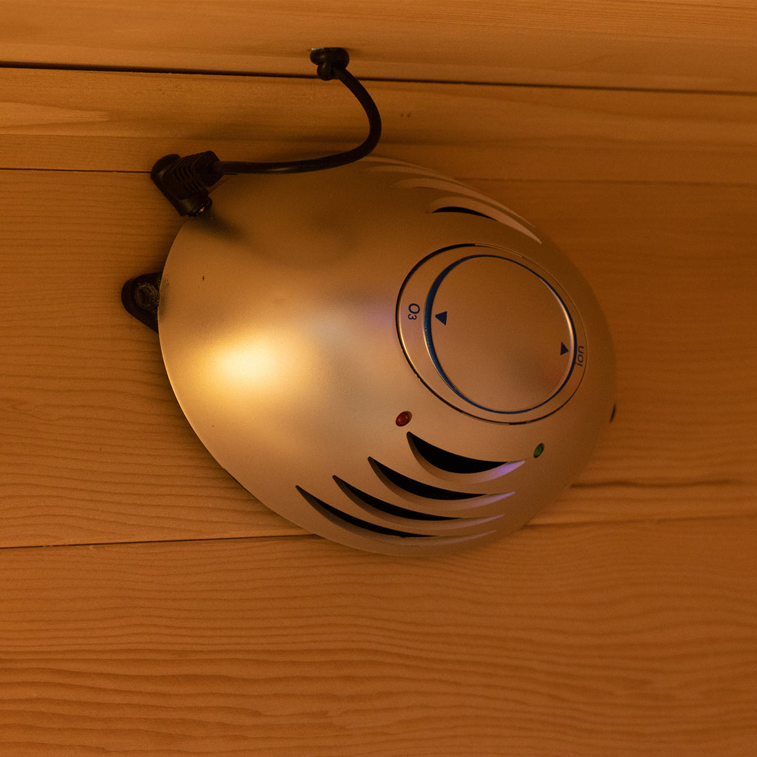 Harlow 1 Person Canadian Hemlock Infrared Home Sauna mounted on wooden paneling, featuring a round silver housing with vents, indicator LEDs, and a dial marked O3 (ozone) and Ion.