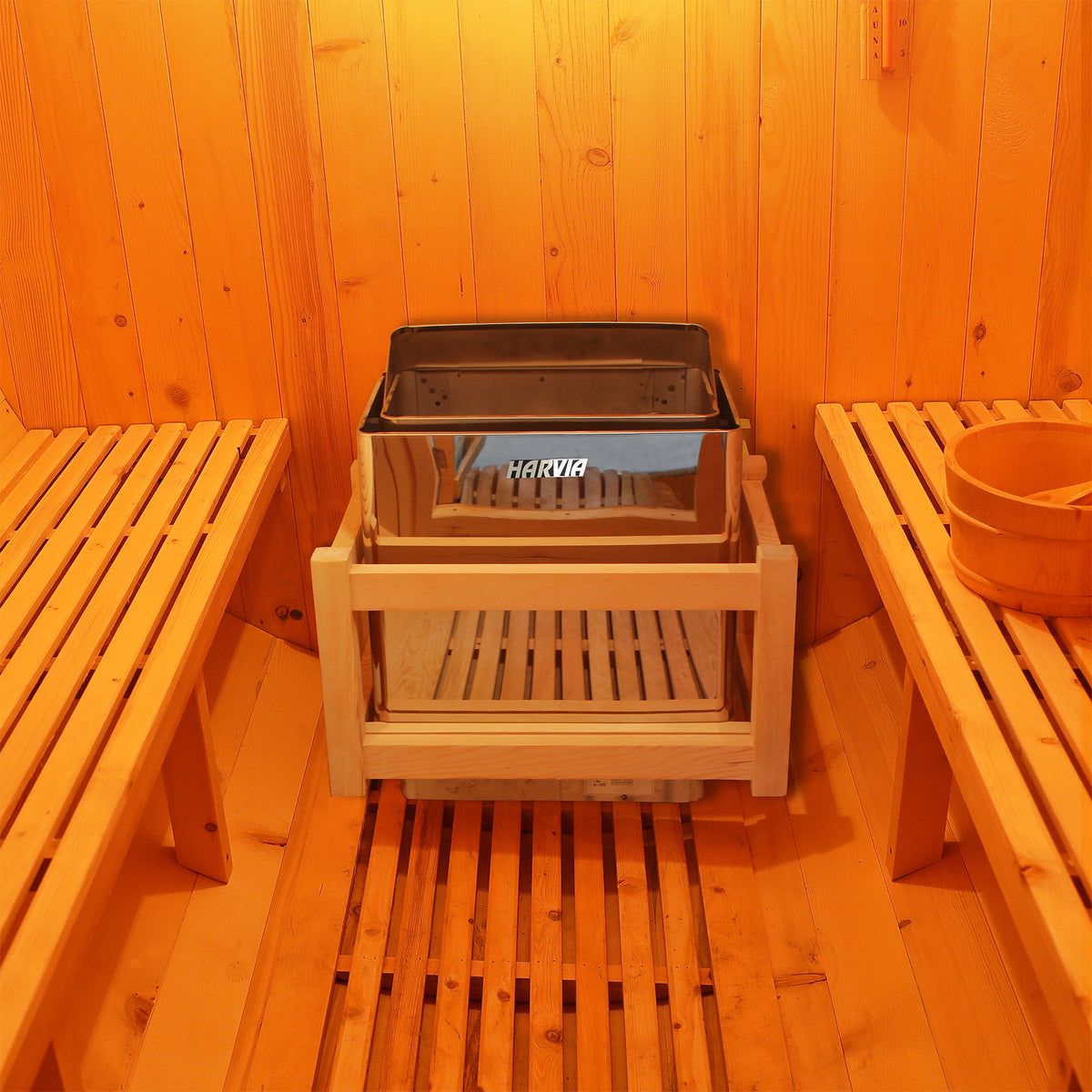 Close-up of the 6kW Harvia Stove Heater for Luola 2 Person Sauna, showcasing its sleek, stainless steel design, positioned beside wooden furniture indoors, emphasizing its durable construction and compact dimensions.