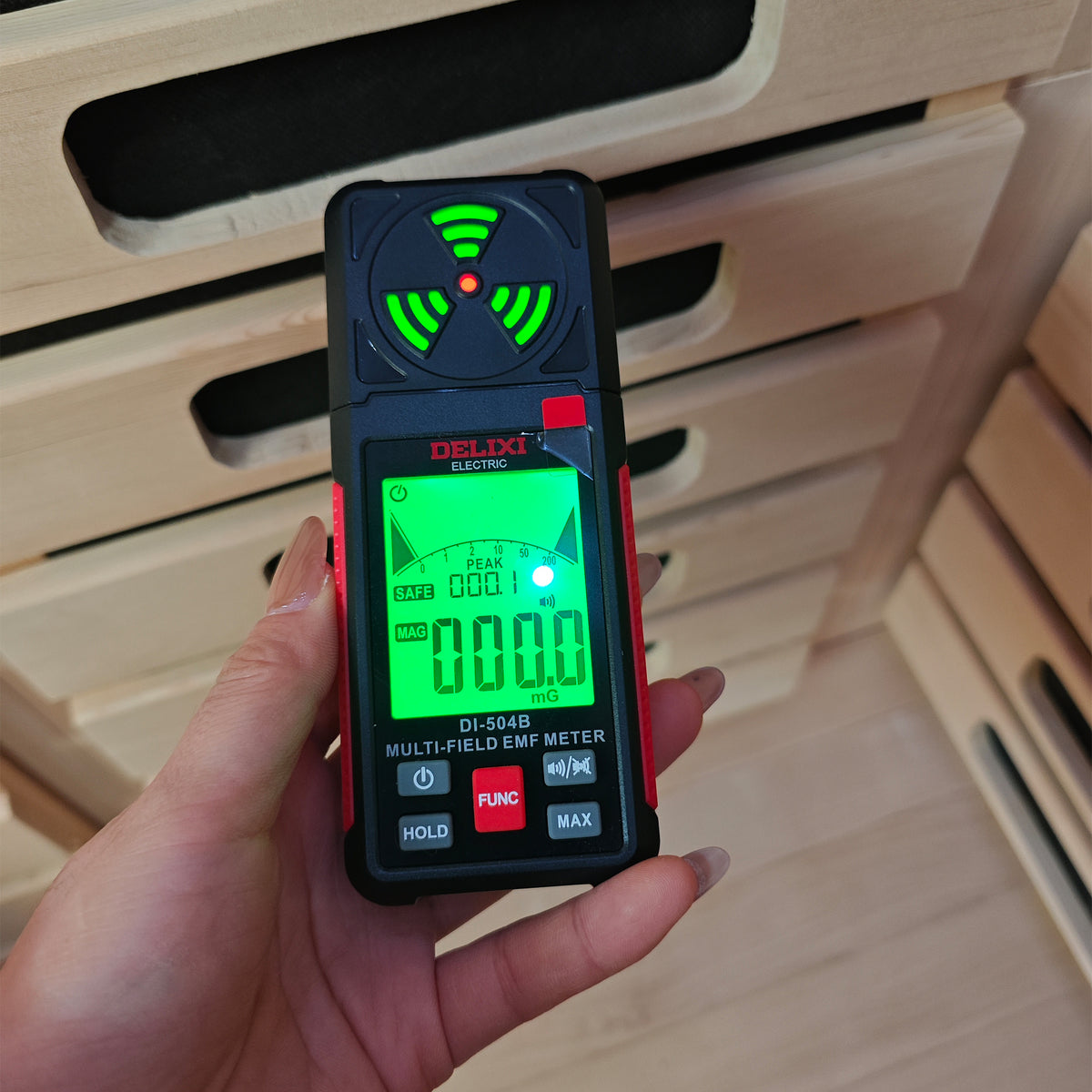 Hand holding EMF meter showing 000.0 mG reading in front of wooden sauna slats
