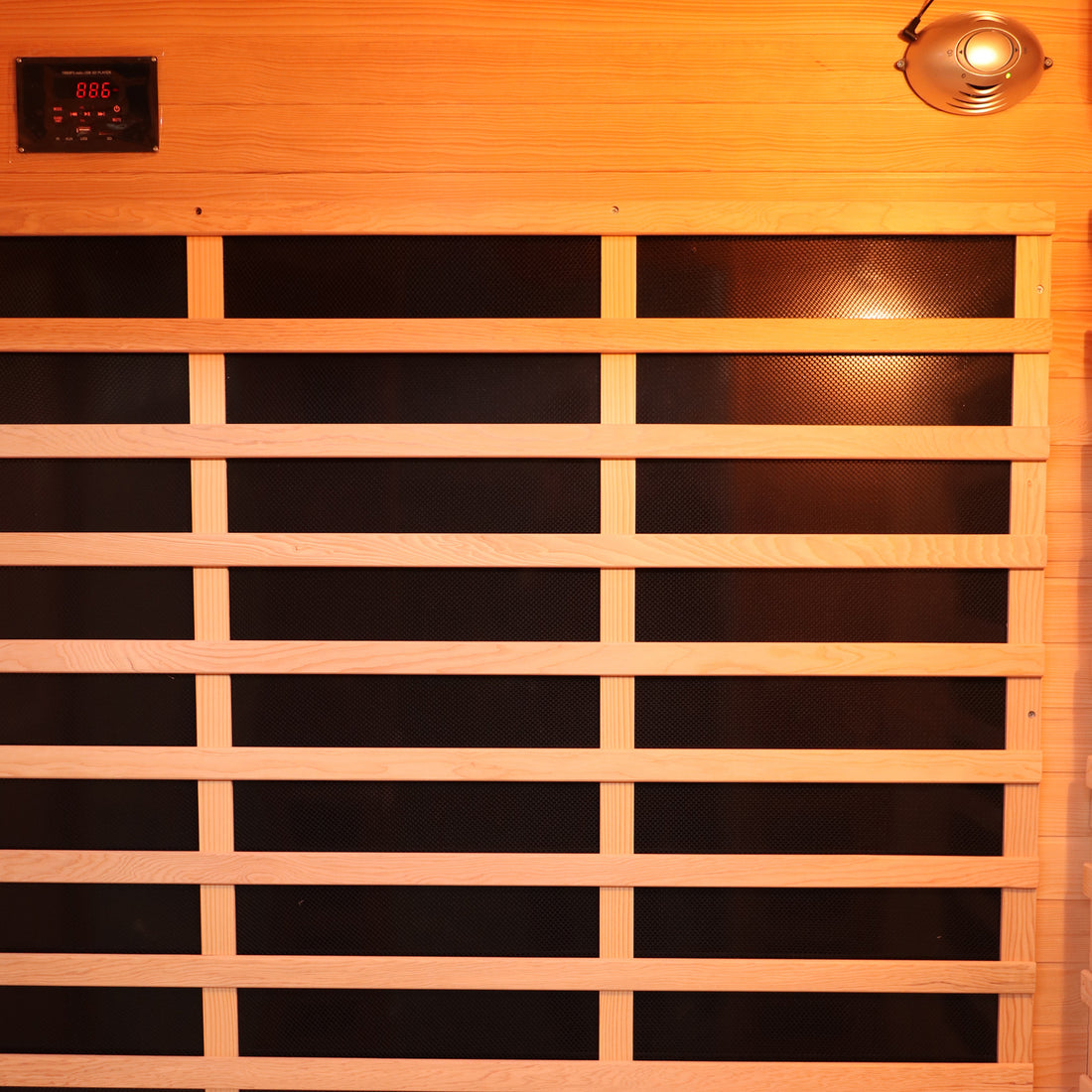 Valo 3 Person Carbon Fibre Infrared Indoor Sauna interior features a black heating panel behind wooden slats, digital control near the ceiling, and a light or speaker fixture, offering luxurious home relaxation.