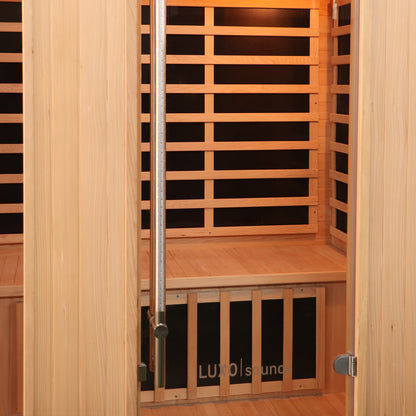 Valo 3 Person Carbon Fibre Infrared Indoor Sauna features a wooden interior with a bench, slatted backrests, infrared heater panels, and a glass door with a stainless steel handle.