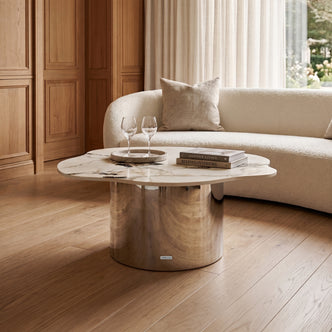 Modern coffee table styled in a living room setting with books, glasses, and a sofa in the background