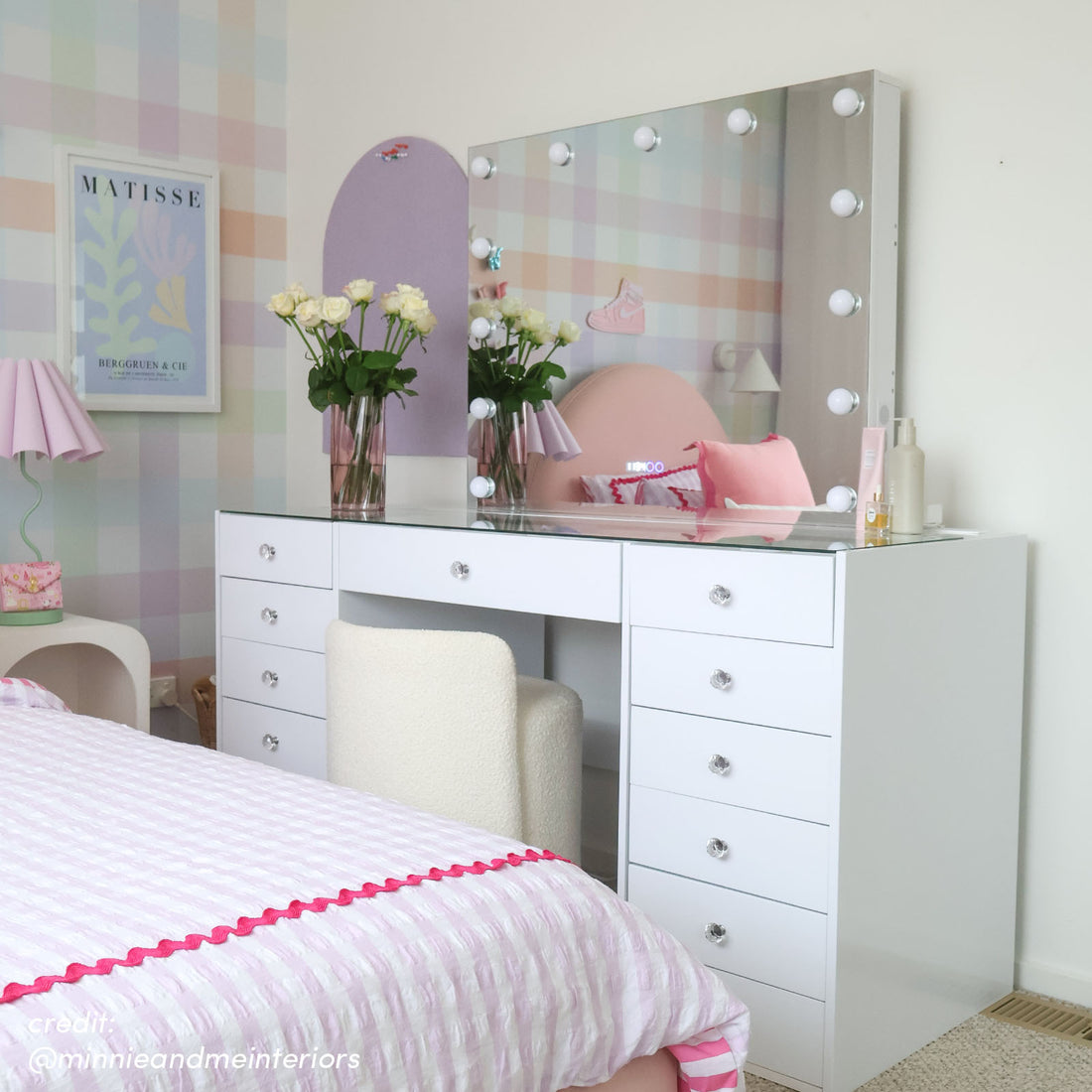 White makeup vanity with Hollywood LED mirror, glass top, crystal drawer knobs, and white boucle stool in a bedroom setting