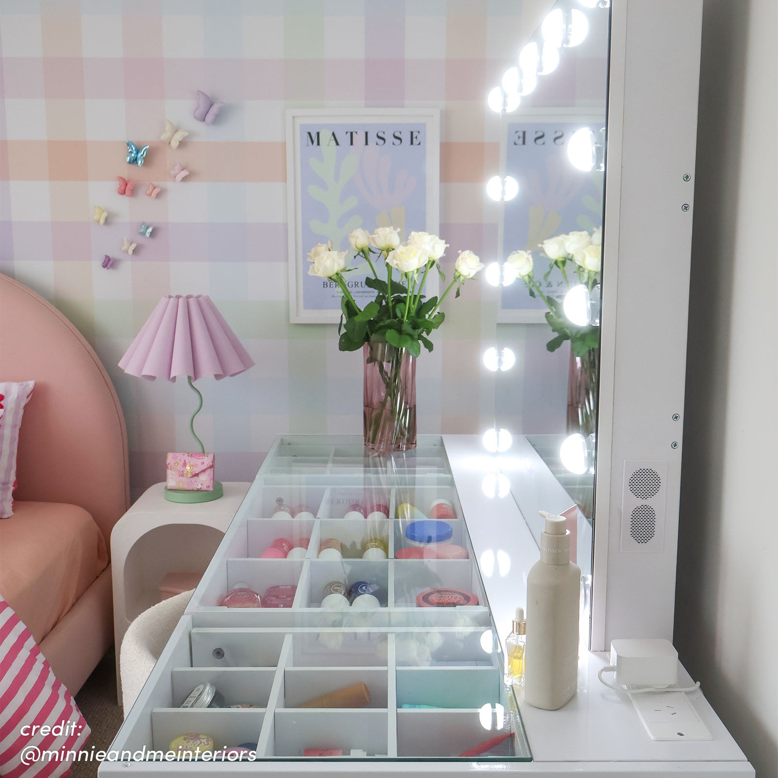 White Hollywood LED vanity with glass-top drawer storage, round bulb mirror and side speakers in a pastel bedroom setting
