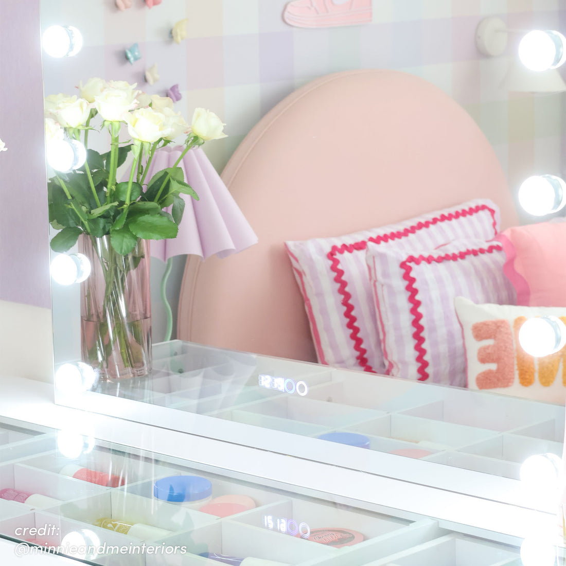 White Hollywood LED vanity mirror reflecting pink bedhead, striped pillows and white roses in glass vase, with glass-top