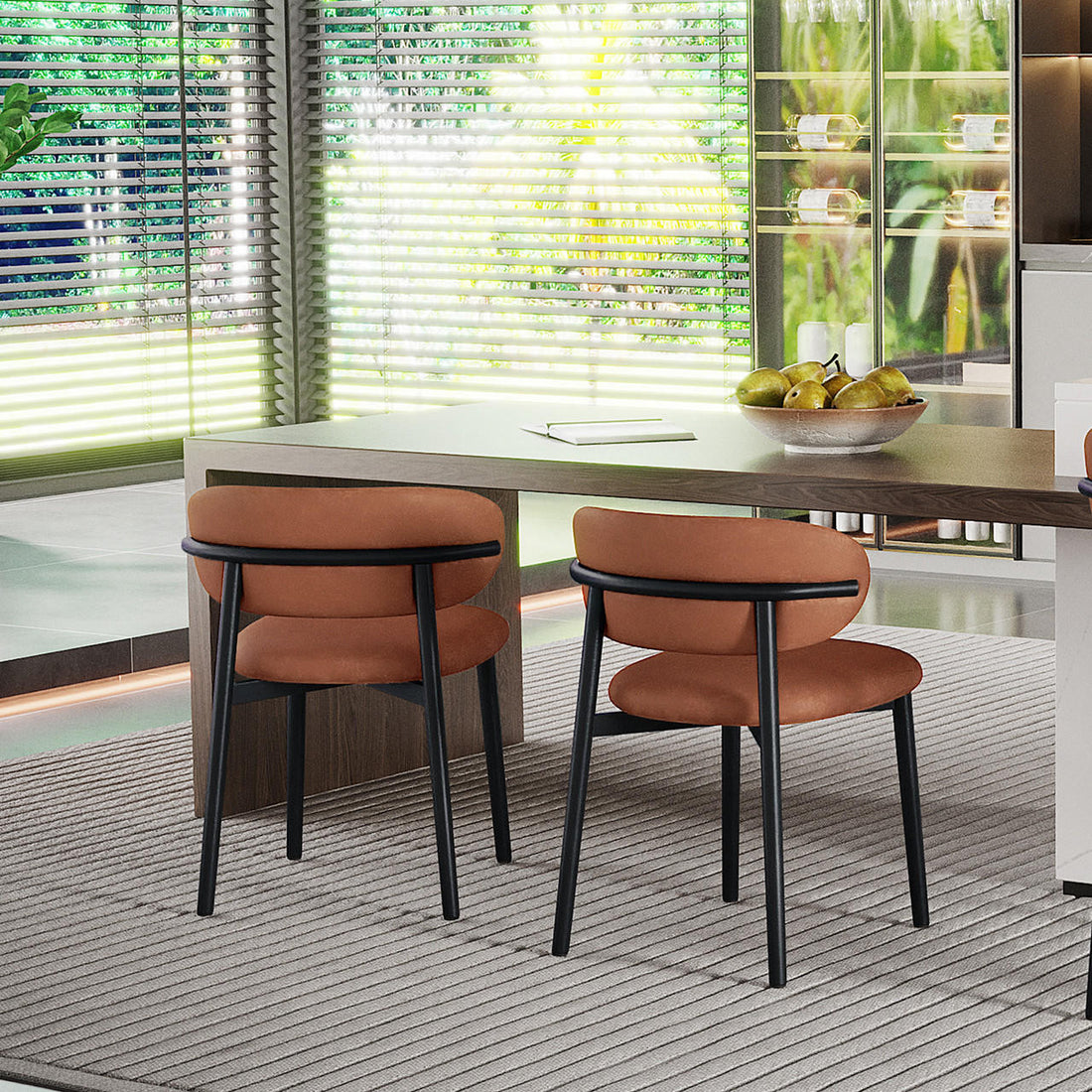 Audrey Curved Leather Dining Chair Set of 2 in Tan features burnt-orange upholstered seats and black metal legs, enhancing a modern room with a wooden table, bowl of pears, and large windows.