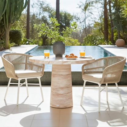 Round travertine concrete dining table with two rope chairs by pool, set with orange juice and pastries