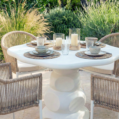 White round concrete outdoor dining table set with wicker chairs, plates, glasses and candles in garden setting
