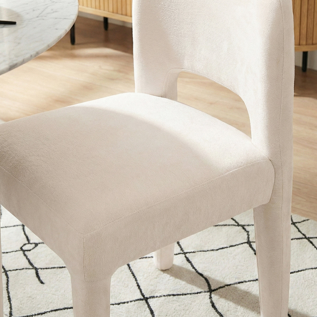 Close-up of Edris dining chair in oat upholstery showing curved backrest and seat detail