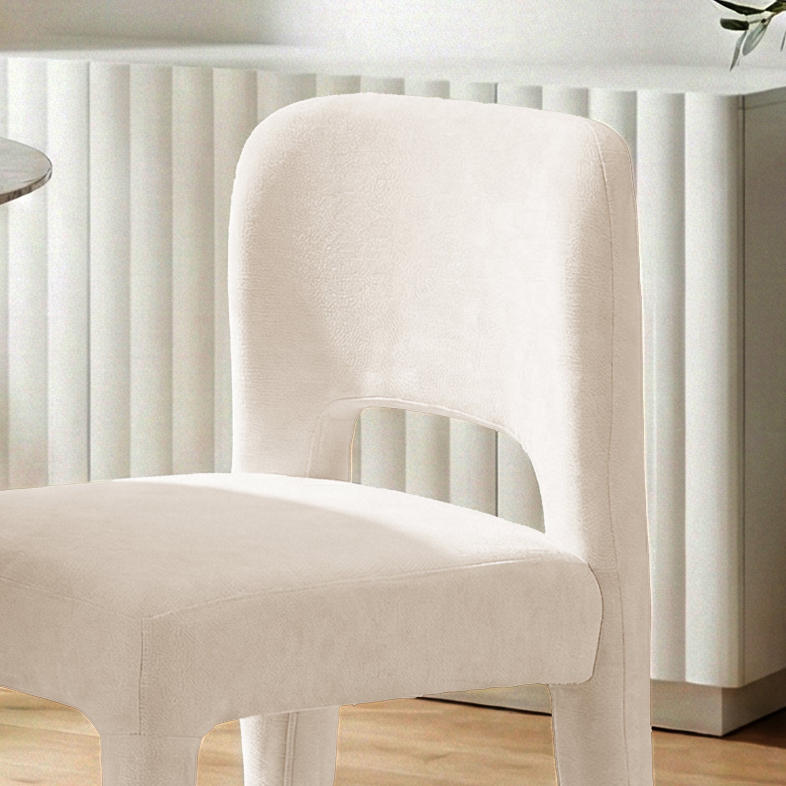 Edris upholstered dining chair in oat fabric with curved backrest and cut-out detail, set against a fluted white wall