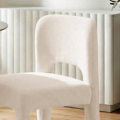 Edris upholstered dining chair in oat fabric with curved backrest and cut-out detail, set against a fluted white wall