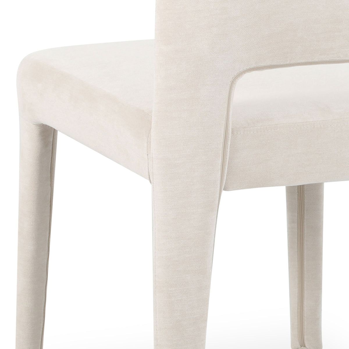 Close-up of Edris dining chair showing upholstered oat fabric, curved backrest with cut-out detail, and padded legs