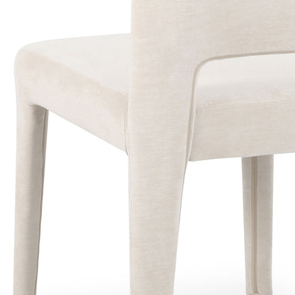Close-up of Edris dining chair showing upholstered oat fabric, curved backrest with cut-out detail, and padded legs