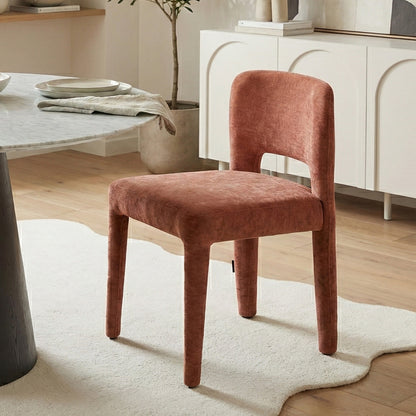 Terracotta upholstered dining chair with curved backrest and cut-out detail, positioned beside a marble-top table on a white