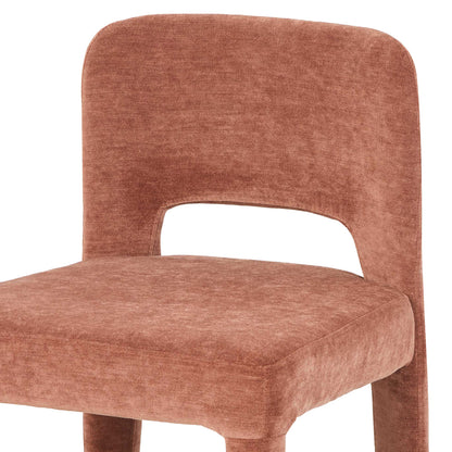 Close-up of terracotta upholstered dining chair with curved backrest and cut-out detail