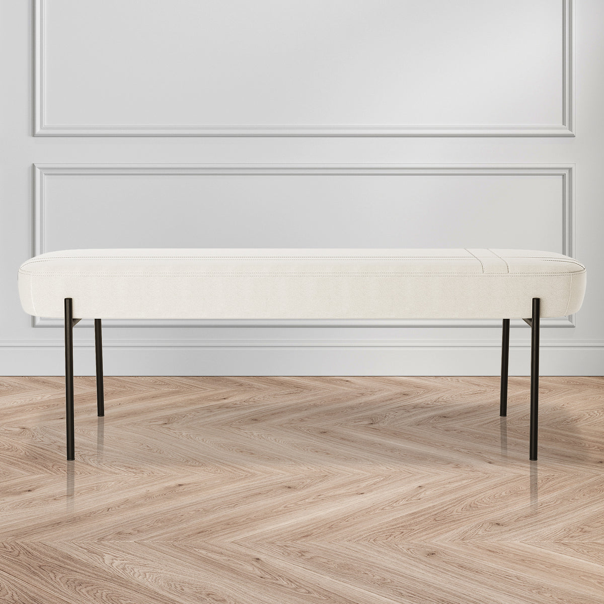 Gavin Dining Bench - Cream White features a minimalist design with a low-profile white cushion and slender black metal legs, set against a white paneled wall on a herringbone-pattern wood floor.