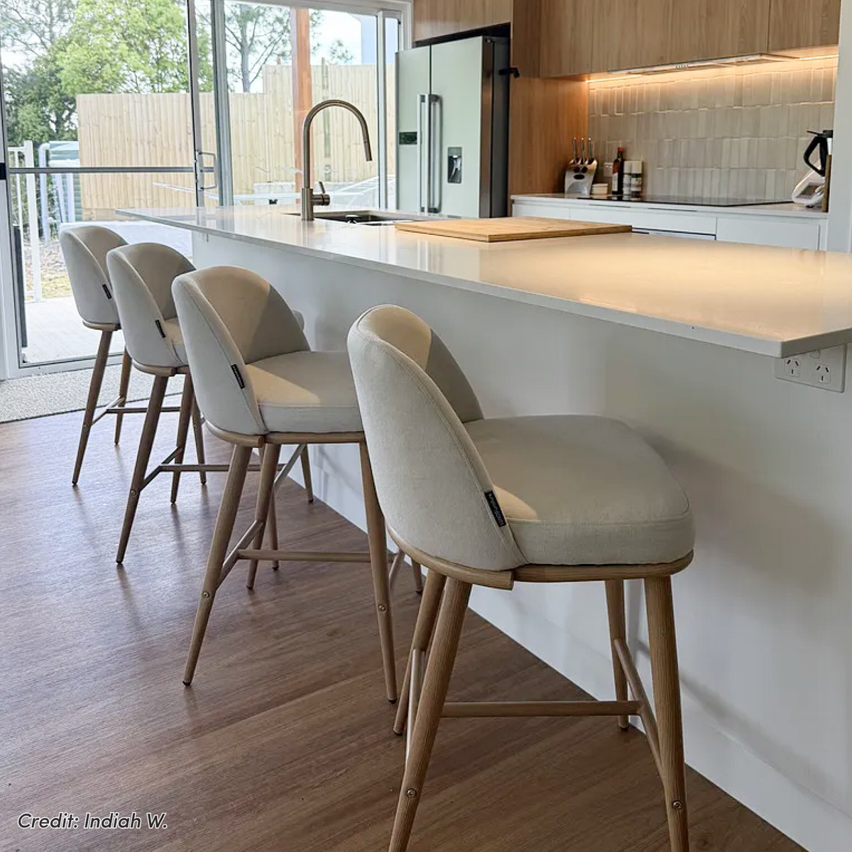 Jeremi high back linen bar stool in wheat with oak legs, shown at a white kitchen island