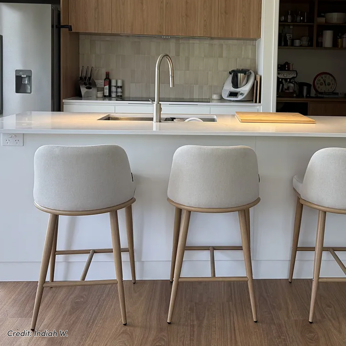 Upholstered bar stools at white kitchen island with timber cabinetry
