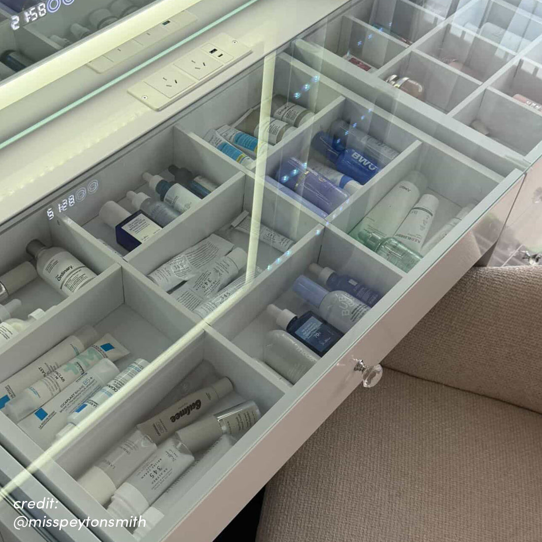 White vanity drawer with LED lighting and organised compartments holding skincare products, featuring crystal knob and power