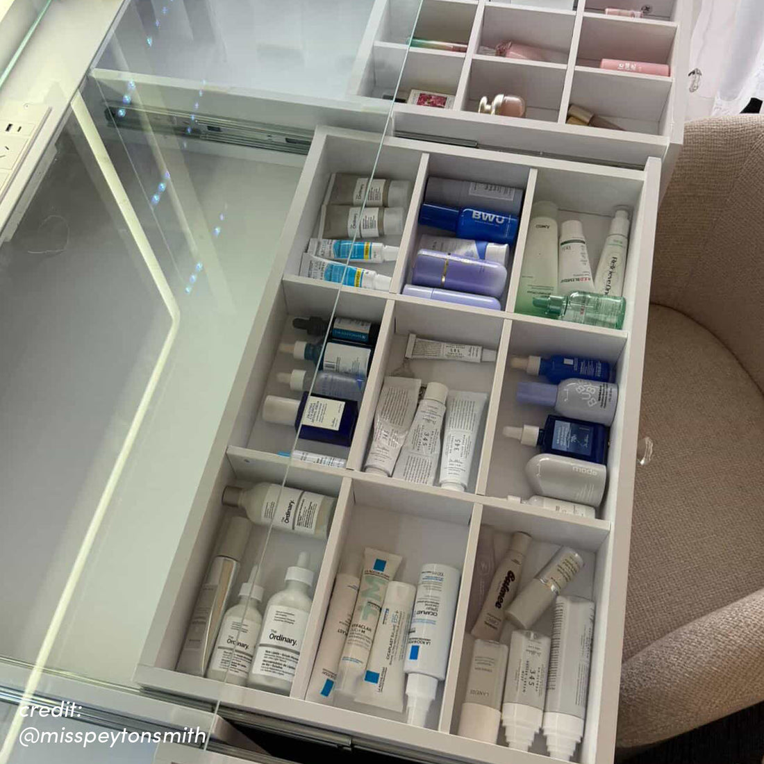 White vanity table with glass-top drawer open revealing organised skincare compartments and illuminated side storage