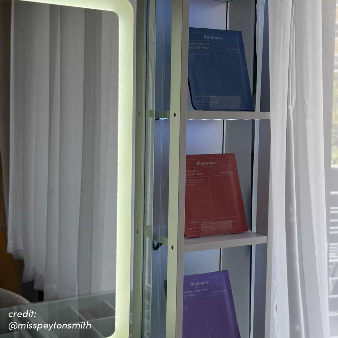 White vanity table with illuminated mirror and glass shelving displaying skincare products