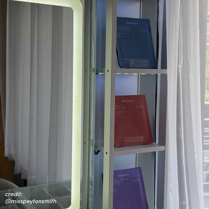 White vanity table with illuminated mirror and glass shelving displaying skincare products