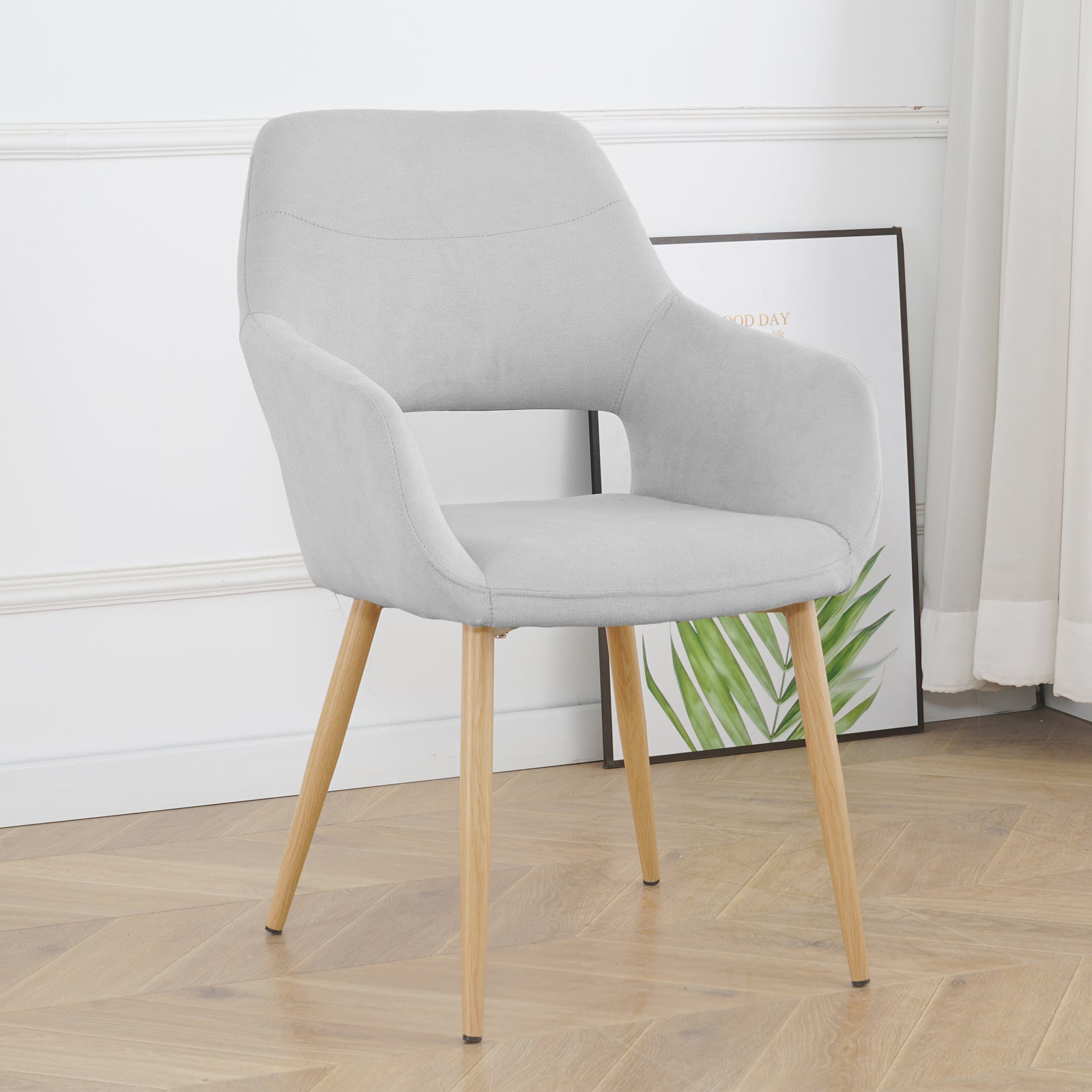 Light grey Keith Fabric Dining Chair Set of 2, featuring a modern upholstered design with a curved backrest, integrated armrests, and four tapered natural-wood legs against a white paneled wall.