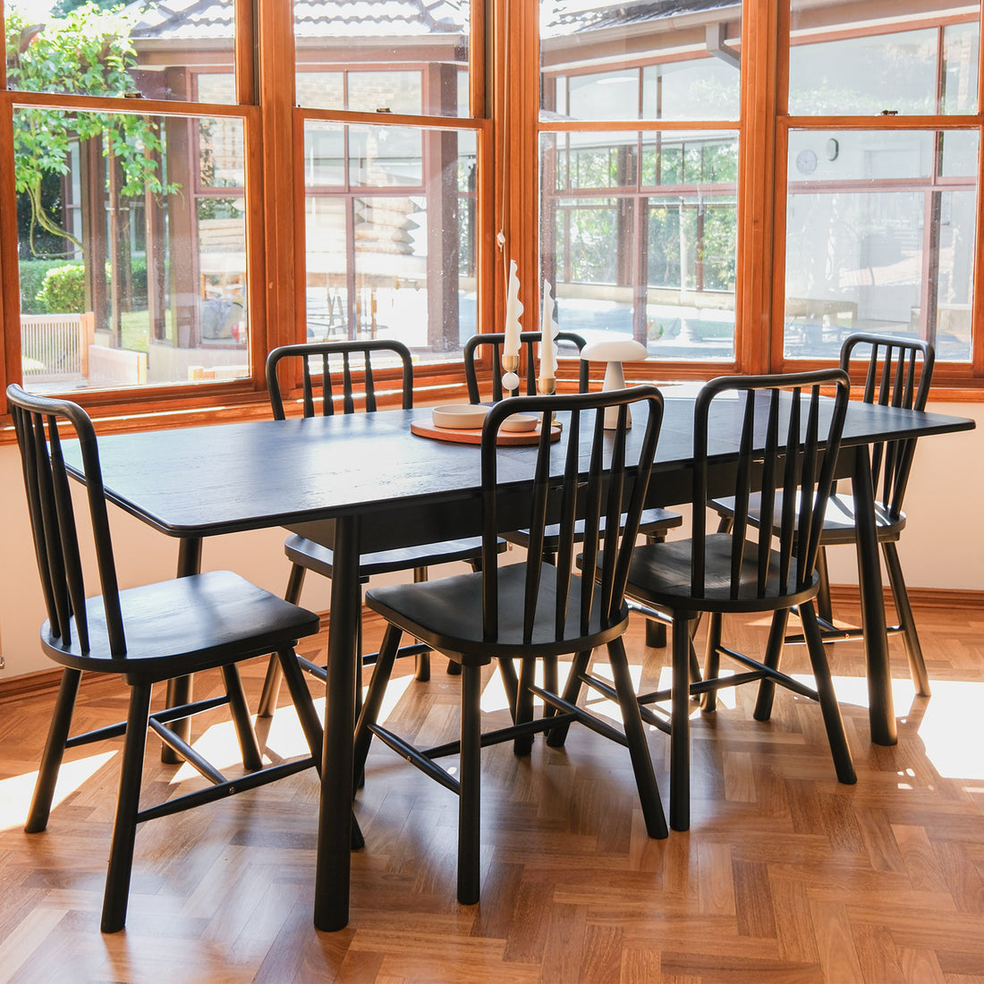 Leigh Solid Oak High-back Dining Chair Black Set of 2, showcased in a sunlit nook with a black wood table, spindle-back design, and natural light from large windows enhancing its modern farmhouse appeal.