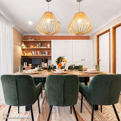 Raynie Velvet Dining Chair Set of 2 in Deep Green features plush velvet upholstery with sleek black metal legs, elegantly arranged around a styled dining table in a modern, light-filled dining room.