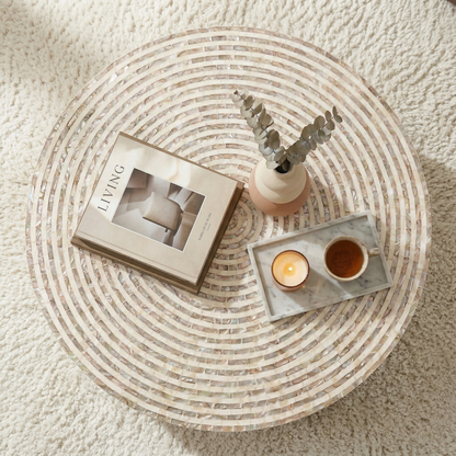 Round Silas Mother of Pearl coffee table in mocha cream with mosaic tile pattern, styled with book, candle, and small vase