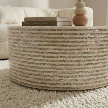 Round mother of pearl coffee table with stacked books and gourd lamp on plush white rug