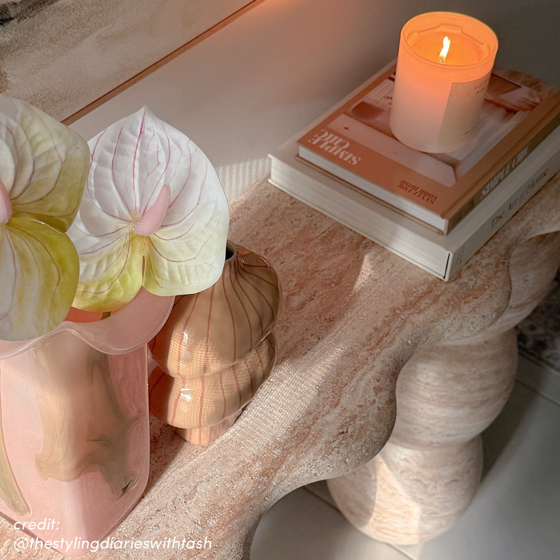 Sculptural travertine console table with curved legs, styled with candle and books