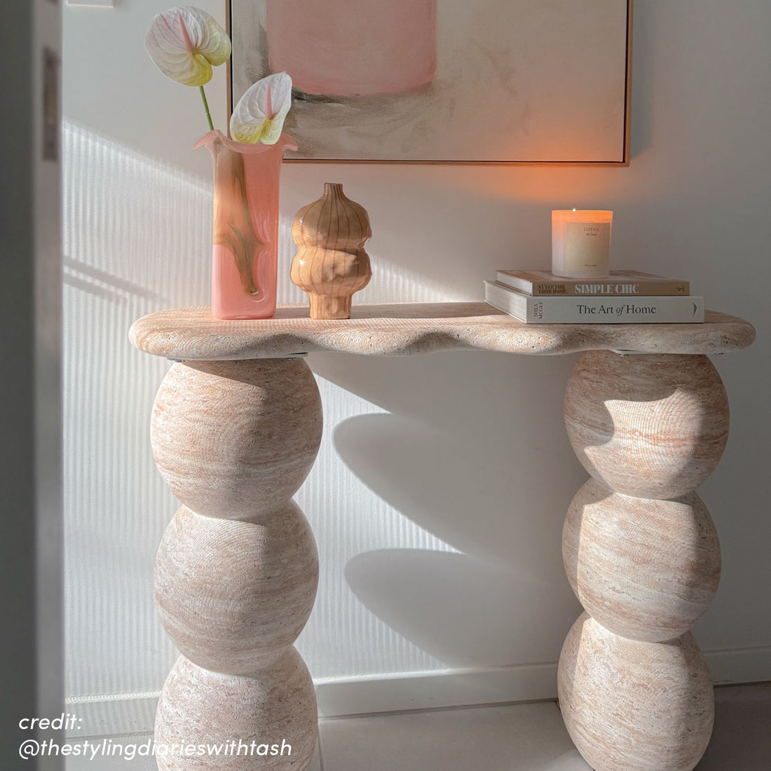Sculptural travertine console table with rounded pedestal legs, displayed with vase, books and candle