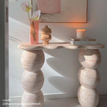 Sculptural travertine console table with rounded pedestal legs, displayed with vase, books and candle