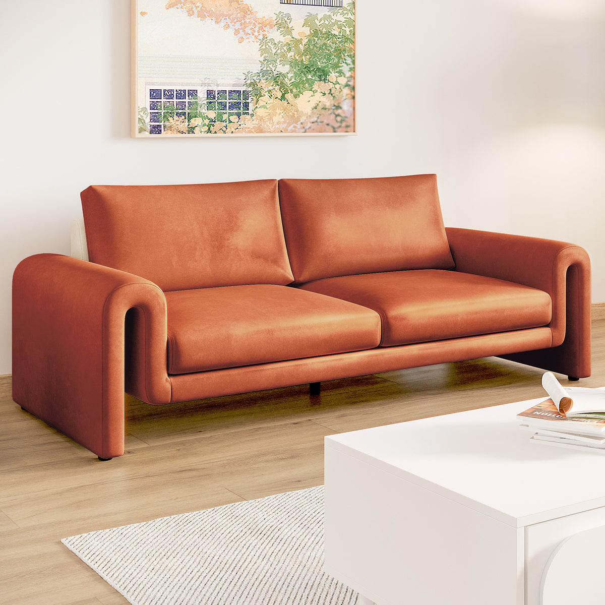 Celyn 3 seater velvet upholstered sofa in burnt orange with curved armrests, shown in a living room with light wood flooring