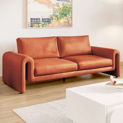 Celyn 3 seater velvet upholstered sofa in burnt orange with curved armrests, shown in a living room with light wood flooring