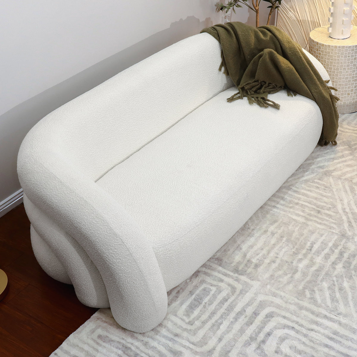 Clioz 3 Seater Curved Boucle Sofa in Eggshell White, featuring soft, rounded edges and nubby fabric, with a dark green throw on one arm, placed on a geometric-patterned rug.