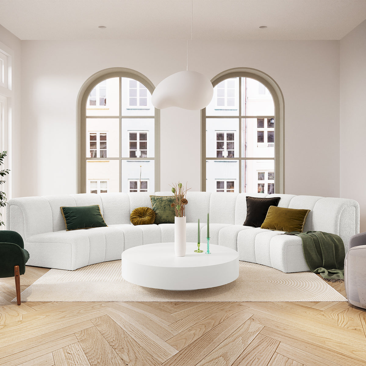 Corina 4 Seater Modular Boucle Sofa in Cream White, featuring a curved design with deep green and mustard accent pillows, set in a bright, minimalist living room with arched windows and parquet flooring.