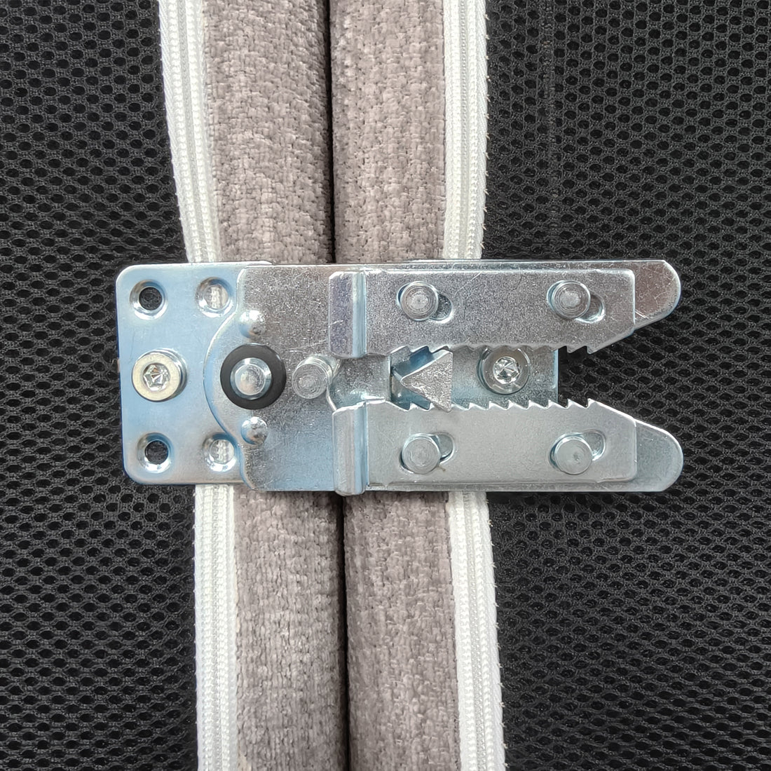 A close-up view of a metal sofa connector bracket, used to securely join modular sofa sections together, attached to the black mesh and taupe fabric underside of the furniture.