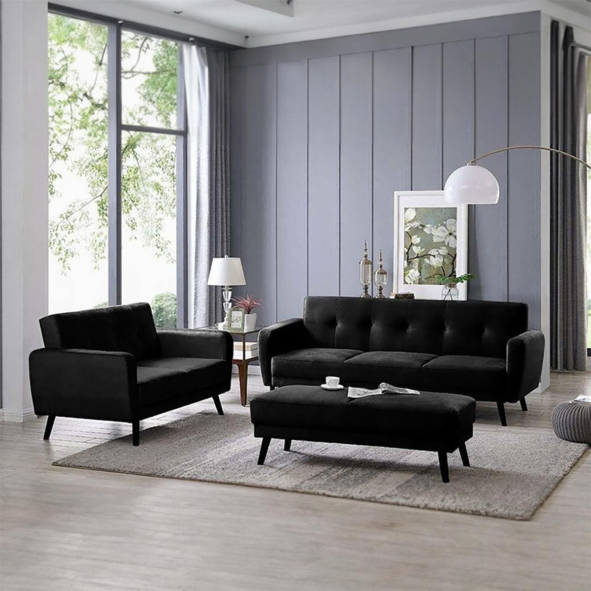 Esben Velvet Fabric Ottoman in Black serves as a coffee table in a modern living room with a matching black sofa set, complemented by Scandinavian-style wooden legs and tufted upholstery.